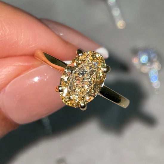 Yellow gold, fancy yellow diamond oval cut ring, held between finger and thumb