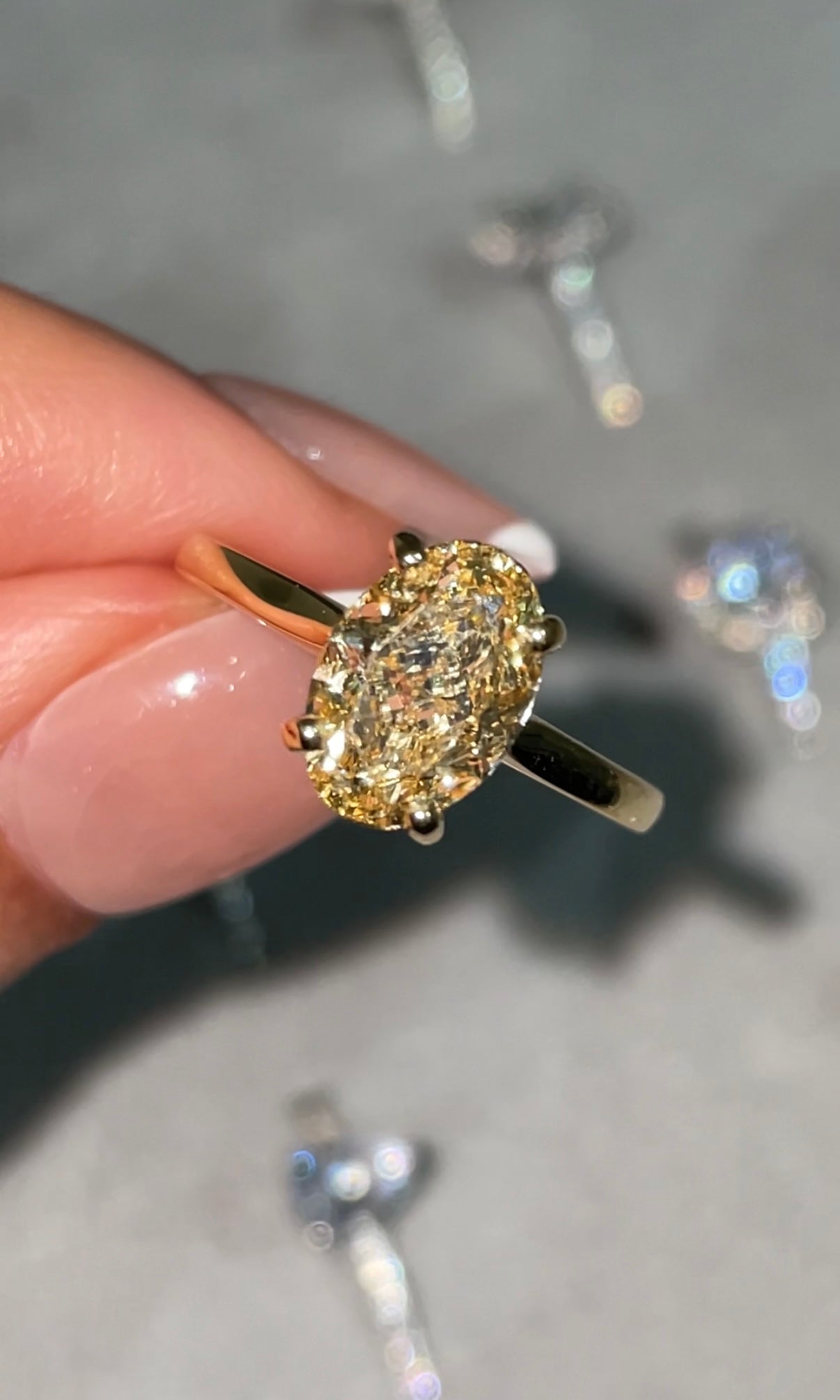 Yellow gold, fancy yellow diamond oval cut ring, held between finger and thumb